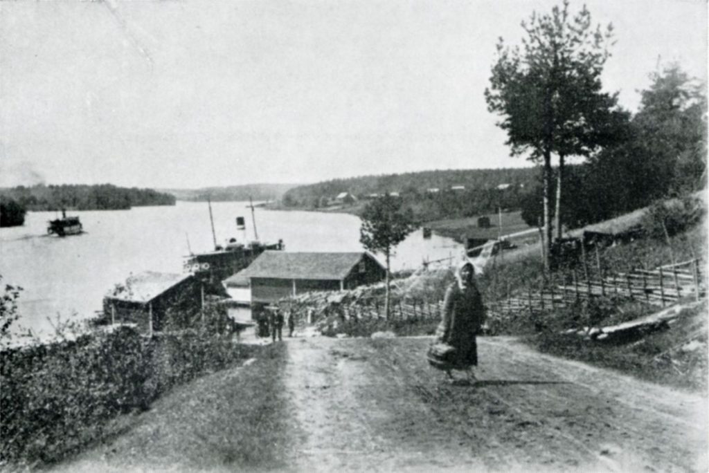 Idyllinen kuva Virtain laivarannasta. Nainen kävelee mäkeä ylös, taustalla kaksi laivaa.